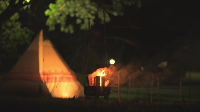 夜のキャンプ場で燃え盛る焚き火の炎と温かく照らされるワンポールテント