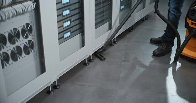 Technician Uses Heavy Duty Vacuum to Clean Tiled Aisle Between Rows of Server Cabinets. Facility Management and Cleanroom Maintenance Ensure Optimal Environmental Conditions For Enterprise Servers.