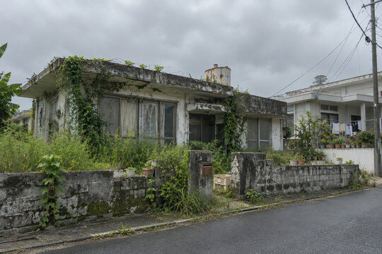 Abandoned house overgrown with weeds under a cloudy sky in Okinawa Japan, vacant property and rural depopulation