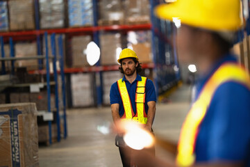 Warehouse worker with a curly beard pushes a manual hand pallet truck along a wide aisle of a...
