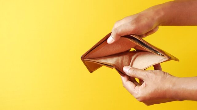 Hands holding and opening empty brown leather wallet, indicating financial hardship, poverty, and unemployment with a vibrant yellow background