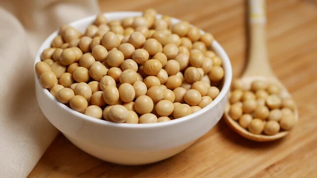 Close up of raw soybeans in white ceramic bowl and wooden spoon on bamboo board with soft cinematic camera motion