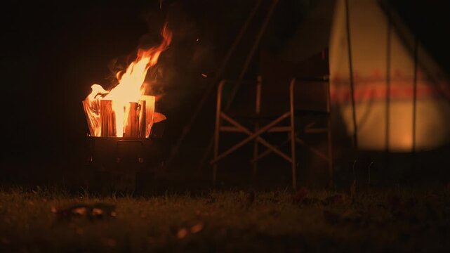 夜のキャンプ場で燃え盛る焚き火の炎と温かく照らされるワンポールテント
