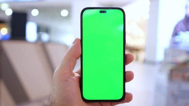 Hand holds smartphone with green screen. Background blurred, indoor setting. Three keyframes show same scene. Phone screen bright green