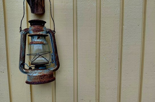 Old rusty kerosene lantern hanging on a yellow wooden paneled wall with copy space