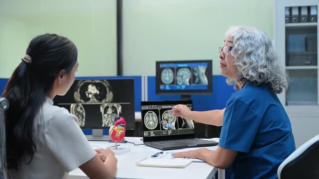 A senior female doctor consults with a young patient, explaining digital MRI body and brain scans on a monitor