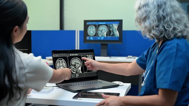 A senior female doctor consults with a young patient, explaining digital MRI body and brain scans on a monitor