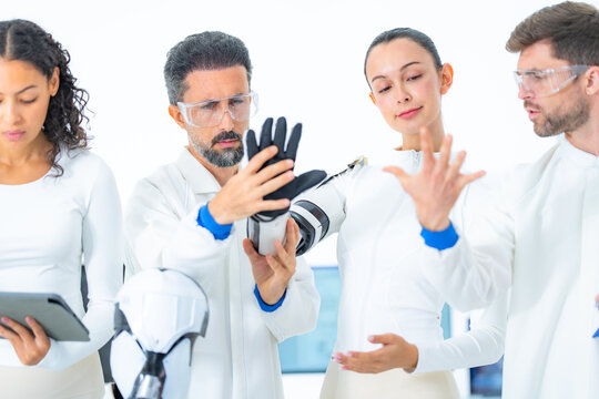 Biomechanics testing lab: a scientist holds a robotic glove aloft while a colleague closes her eyes and mirrors the gesture, sensing the feedback of a haptic trial