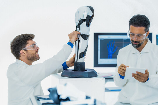 Sensor driven robotics research: a scientist points out a joint encoder on the base of a laboratory robot arm while his colleague keeps a hand on the upper segment
