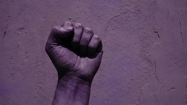 Raised clenched fist pumping against purple textured wall symbolizing protest strength and revolution