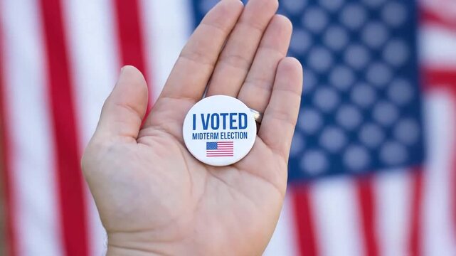Hand holding an I voted midterm election badge against American flag
