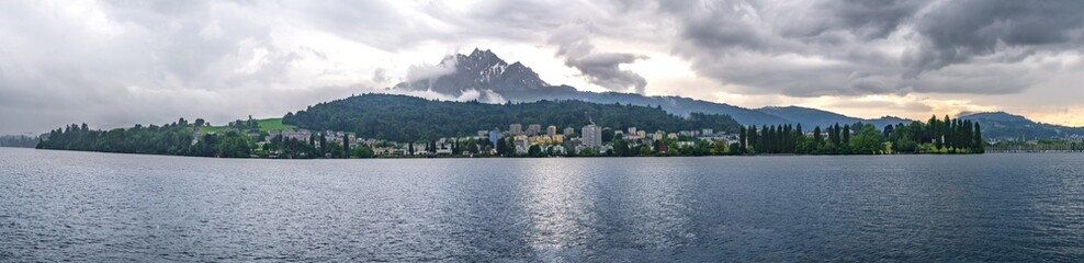 Fototapeta premium Panoramic view of Lake Lucerne shoreline with high-rise buildings and towering mountain in Switzerland