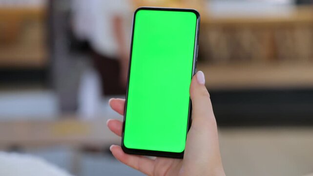 Hand holds smartphone with green screen. Blurred indoor background visible. Three keyframes show slight hand movement. Device has black frame and green display
