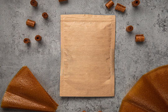 Natural fruit leather rolls and sheets arranged around craft paper ziplock pouch mock up on grey concrete background