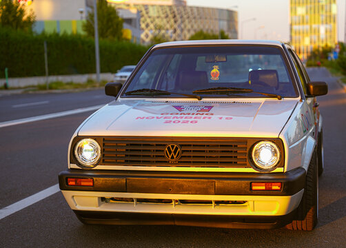 Bucharest, Romania - September 15, 2024: Front view of a white vintage Volkswagen Golf Mk2 classic car parked on an urban street bathed in golden sunset light. GTA concept.