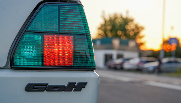 Bucharest, Romania - September 18, 2026: Close-up of a white classic Volkswagen Golf rear tail light illuminated with red brake light during warm sunset golden hour.