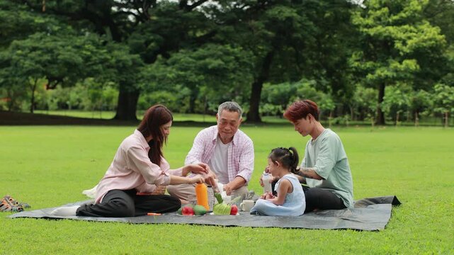 food and drinks. Happy Asian family having fun time on picnic at city nature park, outdoor activitie