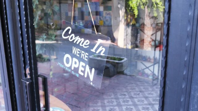 Open sign hanging on glass door of small local business shop during sunny day