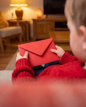 Child in a red sweater holding a red envelope in a warm living room