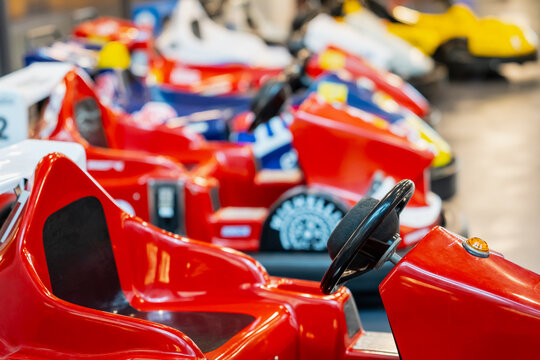 Row of miniature race car vehicles with cockpit seats and manual steering controls, showing ride equipment offered by commercial family recreation facilities
