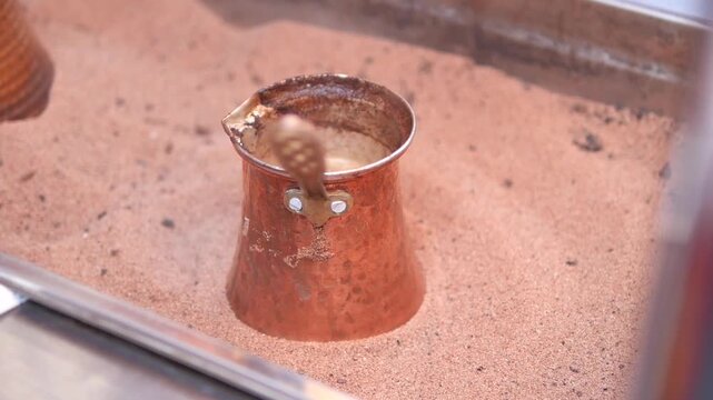 Turkish coffee brewing in hot sand inside traditional copper cezve pot with rising foam