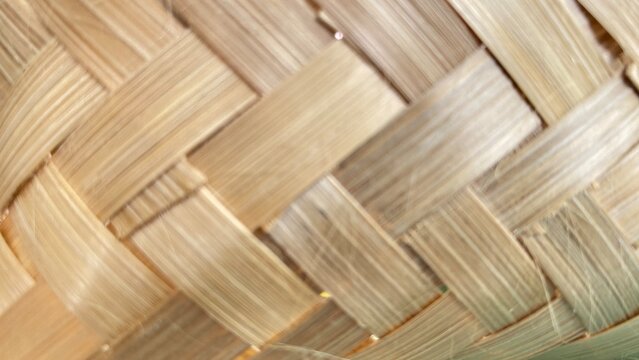 A detailed, close-up shot of a traditional woven bamboo texture showing intricate handcrafting, diagonal interweaving patterns, and natural light-brown wooden fibers. Ideal for background designs, cra
