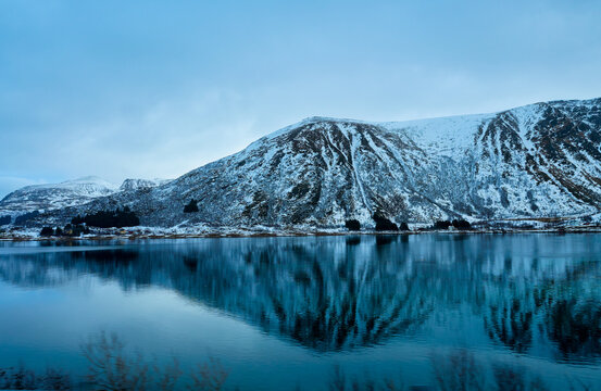 Perfect mountain reflection in calm fjord water during winter in Lofoten Islands, Norway. Scenic Arctic landscape with snow covered peaks and still sea. Beautiful Nordic nature background for Scandina