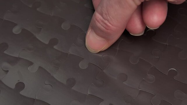 Human hand completing black jigsaw puzzle putting last final piece close-up, successful solution of problem