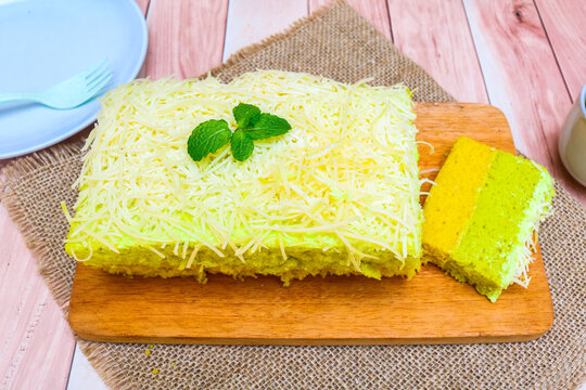 Delicious avocado flavored cake topped and filled with creamy frosting, generously covered with fine shredded cheese served on a wooden board with a slice showing the soft green cake texture.