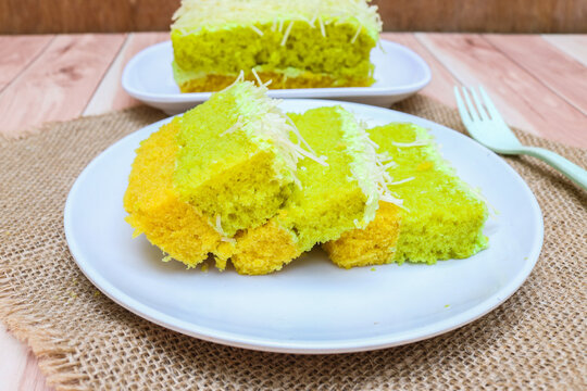 A slice of soft green avocado flavored cake topped and filled with creamy frosting, generously covered with fine shredded cheese served on a white plate