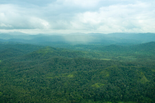 Aerial view of endless tropical rainforest and mountain ranges with rain pouring down in the distance, Kelabit Highlands, Borneo