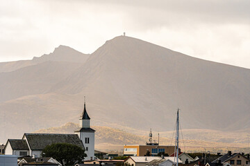 Nordic village with white church spire in front of a majestic mountain under warm sunlight © Quality by Simon