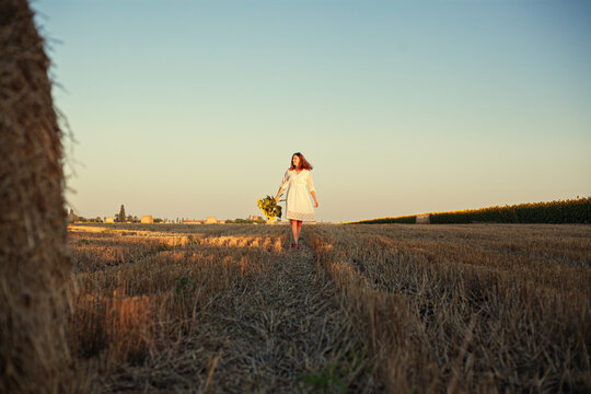 woman in a white dress holding a bouquet of wild flowers with sunflowers in a field