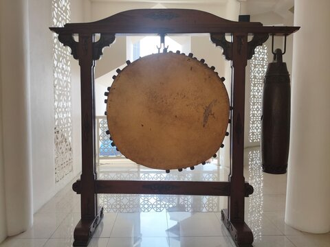 A traditional Indonesian Bedug drum with a hanging wooden instrument called " kenthong " inside a mosque, showcasing cultural heritage and woodwork craftsmanship.
