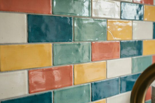 A close up of a kitchen or bathroom wall tiled with rectangular ceramic tiles in various colors including blue, green, yellow, and terracotta red