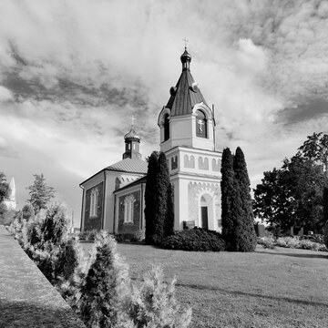 Monochrome architectural shot of an Orthodox church with a bell tower and decorative thuja trees