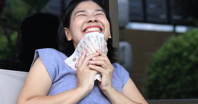 Happy young woman smiling while holding cash, expressing financial success, savings, income, profit, wealth, positive lifestyle, personal finance, and economic achievement