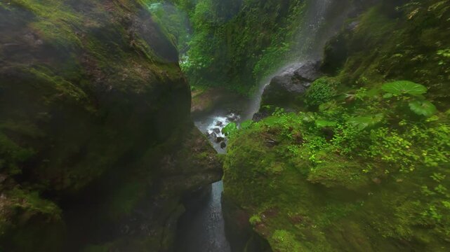 FPV drone flight through misty Costa Rica rainforest canyon where a group of people descend down the river past mossy boulders turquoise pools whitewater rapids and lush tropical greenery.