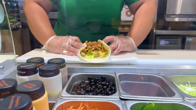 A chef prepares a delicious burrito, carefully folding tortilla with a variety of fresh ingredients and sauces on white counter in a restaurant kitchen.