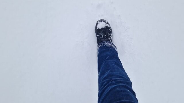 Top view of legs in winter boots and jeans walking through deep white snow. Video shows first person movement during a winter walk or hike. Close-up of legs making a path through fresh snow