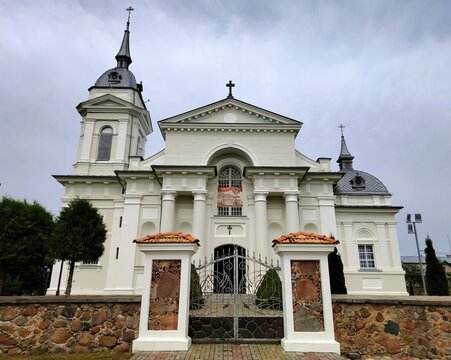 Symmetric facade of a white Catholic church with classical columns, bell towers and a stone wall