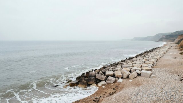 Rock armour boulders defending a shingle shore under flat overcast light