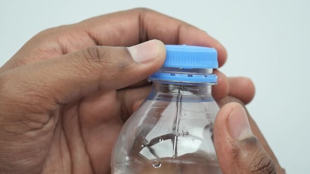 A close up view of person's hands opening a small plastic water bottle with blue cap, clear liquid visible
