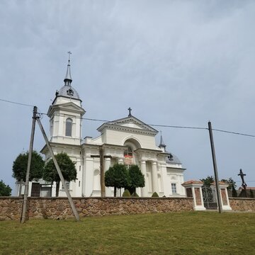 Low angle view of the Holy Trinity Catholic Church facade with columns and a stone wall under cloudy sky