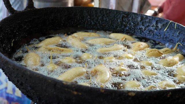 Deep frying snacks or fritters in boiling oil in large black iron kadai pan