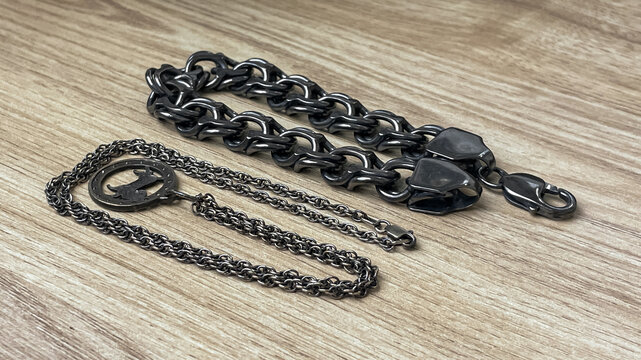 Two silver chains with different link styles and a decorative pendant lie on a wooden surface. The darkened metal indicates a need for cleaning and maintenance.