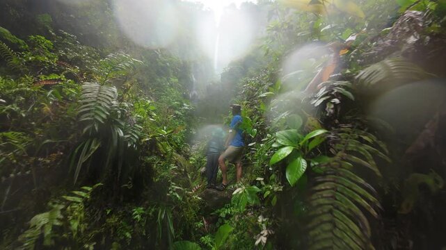 FPV drone flight over misty rainforest canyon waterfall in Costa Rica with turquoise river below lush ferns and moss covered cliffs a wild route explored by father with son on holiday.
