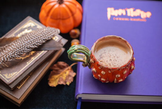 Cozy autumn still life featuring cappuccino in a ceramic pumpkin mug sprinkled with chocolate and cinnamon, surrounded by books on a green velvet background. Seasonal coffee and reading concept 