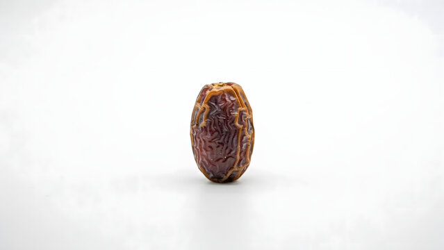 A single dried date fruit with a wrinkled brown skin and a textured surface isolated on a plain white background, for food