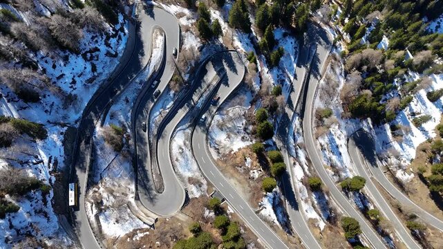 malojaschlange switchbacks descend wooded slope bus cars truck round tight loops patchy snow rocky terrain maloja pass drone footage overhead graubunden switzerland